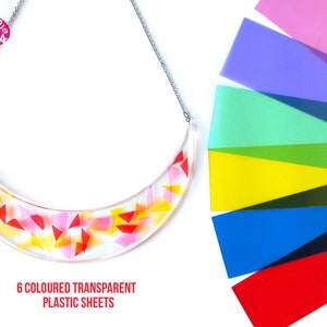 Puede incluir: Un collar de plástico transparente con forma de media luna y un diseño geométrico colorido. El collar está hecho con seis láminas de plástico transparente en rojo, rosa, amarillo, verde, azul y morado. El texto "6 COLOURED TRANSPARENT PLASTIC SHEETS" está debajo del collar.