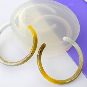May include: Two yellow and white resin hoop earrings with black flecks. The earrings are on a clear silicone mold. Handmade in Italy.