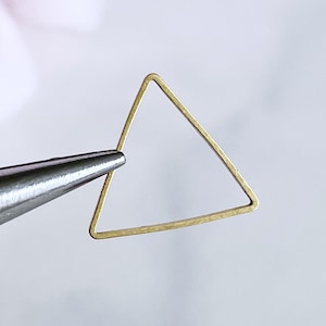 Puede incluir: Un anillo de metal de forma triangular dorada, sostenido por unas pinzas.