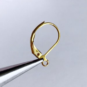 Könnte beinhalten: Goldfarbener Ohrringhaken mit einer kleinen Schlaufe am unteren Ende. Der Haken wird von einer Zange gehalten.