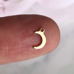 May include: A small gold crescent moon charm with a hole at the top for attaching to jewelry.