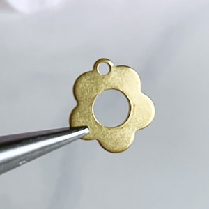 May include: A gold-colored metal flower charm with a hole in the center. The charm is in the shape of a simple flower with five petals.