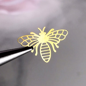 May include: Gold metal bee cutout, a delicate and intricate design with a detailed body and wings.