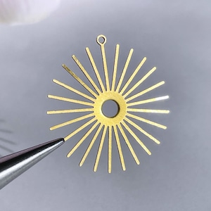 May include: Gold metal sunburst charm with a hole in the center for attaching to jewelry or other crafts.