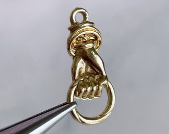 May include: Gold-toned metal charm featuring a hand holding a ring. The charm has a loop at the top for attaching to a necklace or bracelet.
