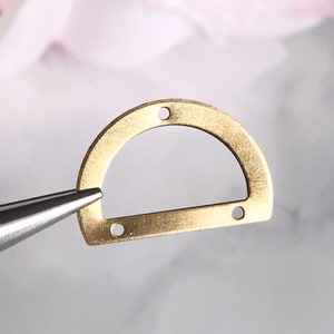 May include: A gold-colored metal D-ring with four holes for attaching jewelry or other crafts.