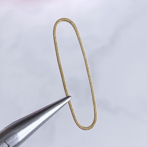 Puede incluir: Un anillo de salto ovalado de oro, un anillo de metal utilizado en la fabricación de joyas, está sujeto por unas pinzas.
