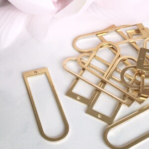 May include: A pile of gold-colored metal frames, some are rectangular and some are oval shaped. The frames are on a white surface.