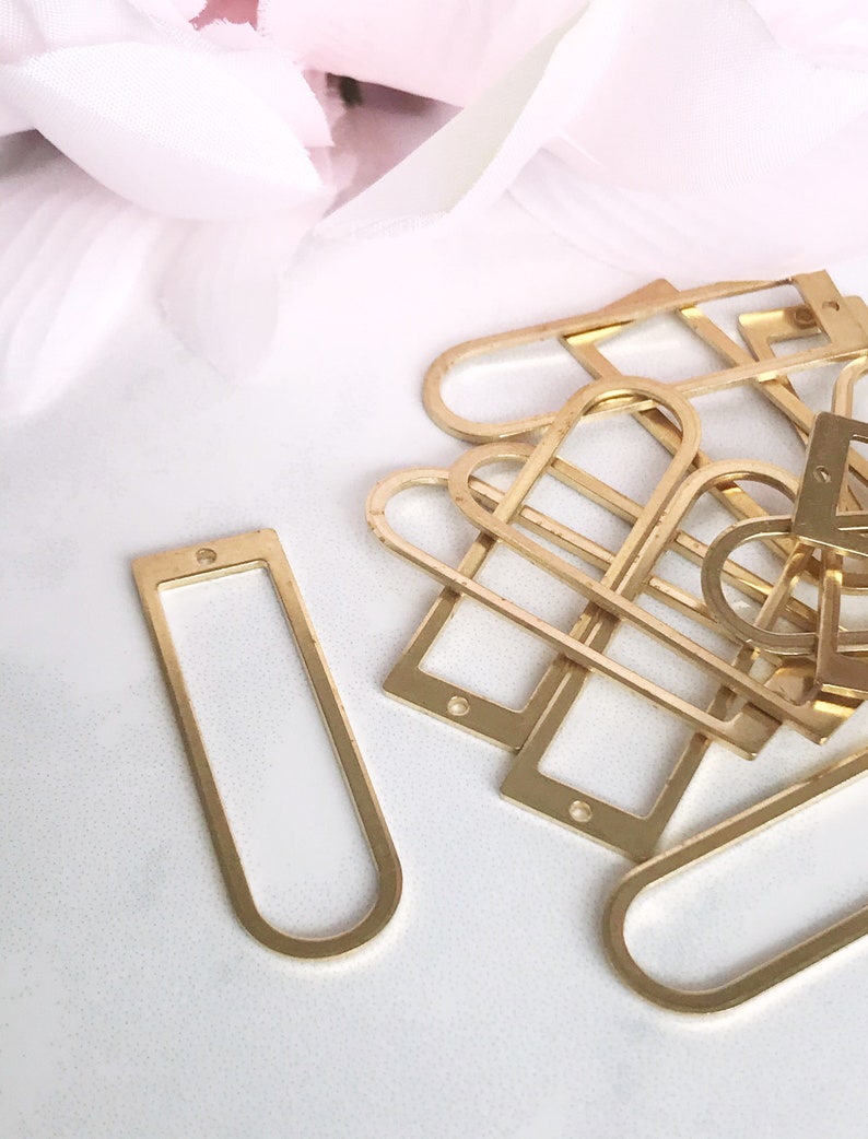 May include: A pile of gold-colored metal frames, some are rectangular and some are oval shaped. The frames are on a white surface.
