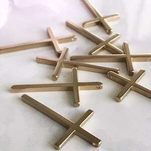 May include: A group of gold-colored metal cross charms. The crosses are simple in design and have a flat, rectangular shape.