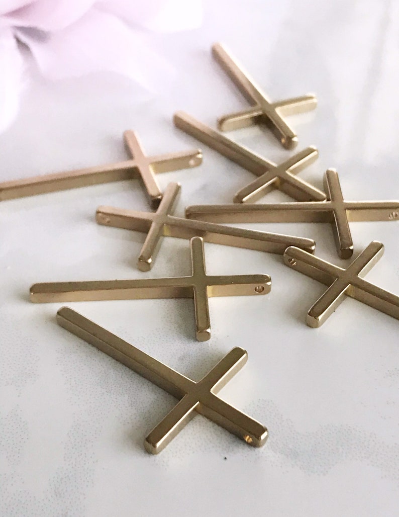 May include: A group of gold-colored metal cross charms. The crosses are simple in design and have a flat, rectangular shape.