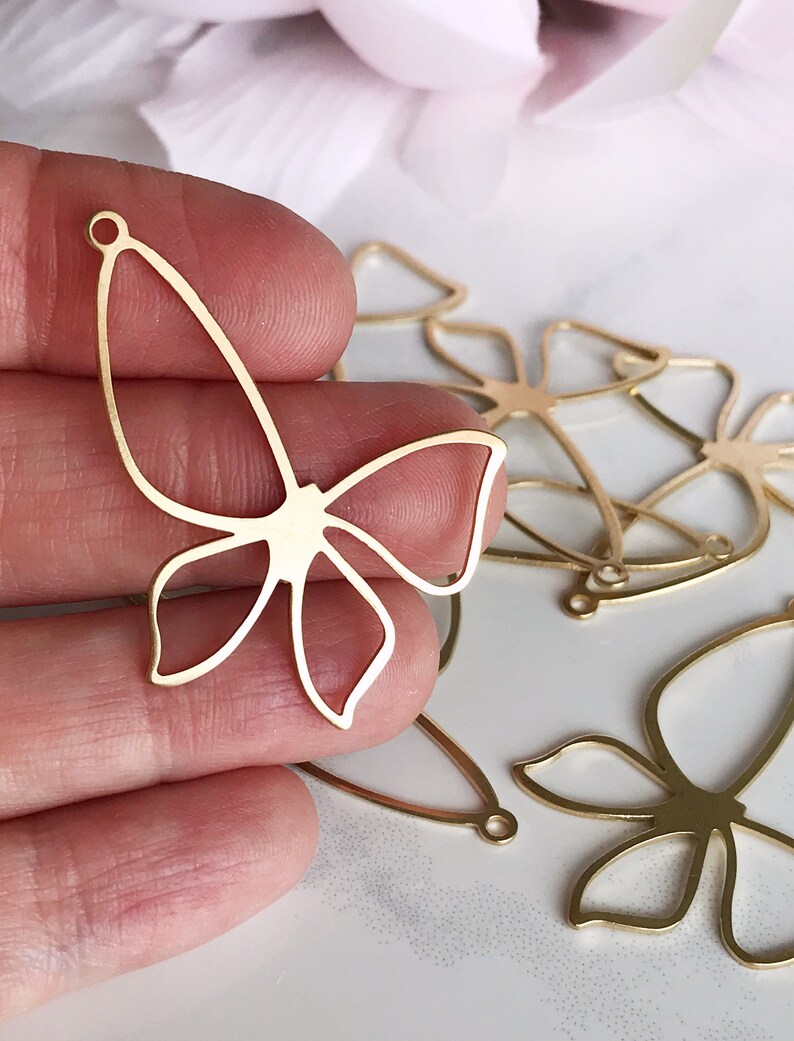 May include: Gold metal butterfly charms with a delicate cutout design. The charms have a hole at the top for attaching to jewelry or other crafts.