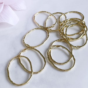 May include: A set of 10 gold-toned metal rings with a hammered texture. The rings are oval shaped and are arranged in a pile.