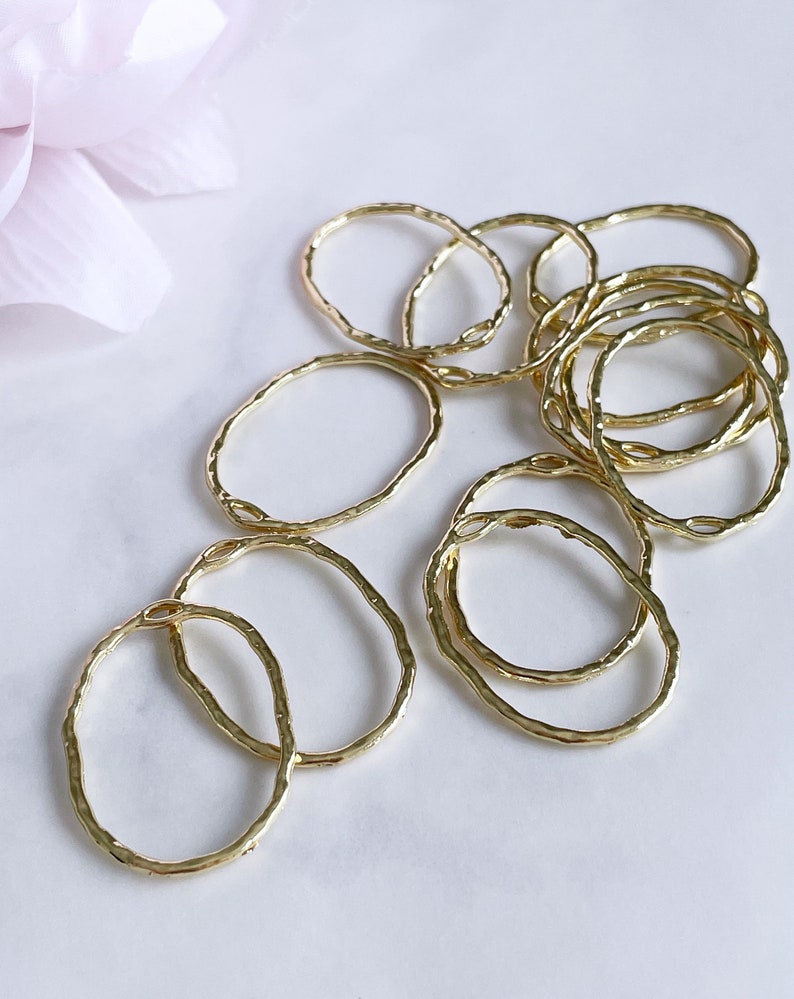 May include: A set of 10 gold-toned metal rings with a hammered texture. The rings are oval shaped and are arranged in a pile.