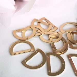 May include: A pile of gold-colored metal half-circle D-ring hardware with small holes around the edges.