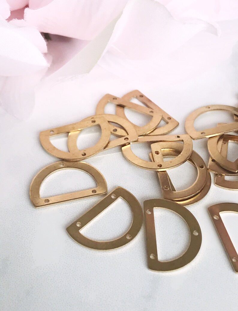 May include: A pile of gold-colored metal half-circle D-ring hardware with small holes around the edges.