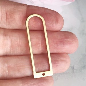 May include: Gold-toned metal frame with a rounded top and a small hole at the bottom. The frame is rectangular with a slightly rounded top and bottom.