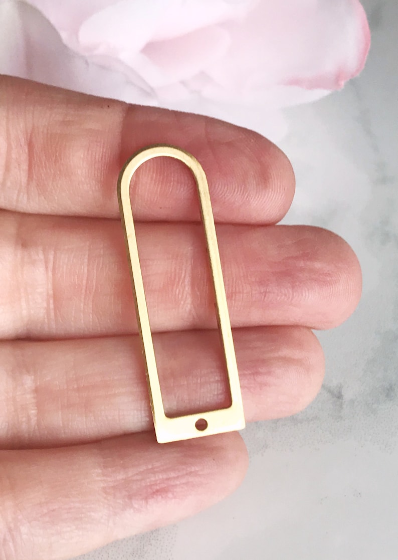 May include: Gold-toned metal frame with a rounded top and a small hole at the bottom. The frame is rectangular with a slightly rounded top and bottom.