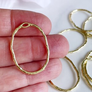 May include: Gold oval-shaped metal rings with a textured surface. The rings have a small opening at the top.