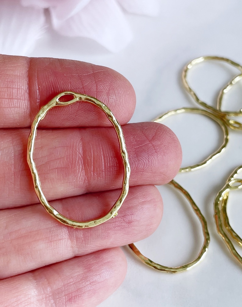 May include: Gold oval-shaped metal rings with a textured surface. The rings have a small opening at the top.