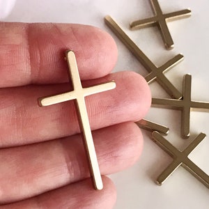 May include: A set of five gold-toned metal cross charms. The crosses are simple and elegant, with a flat, rectangular shape.