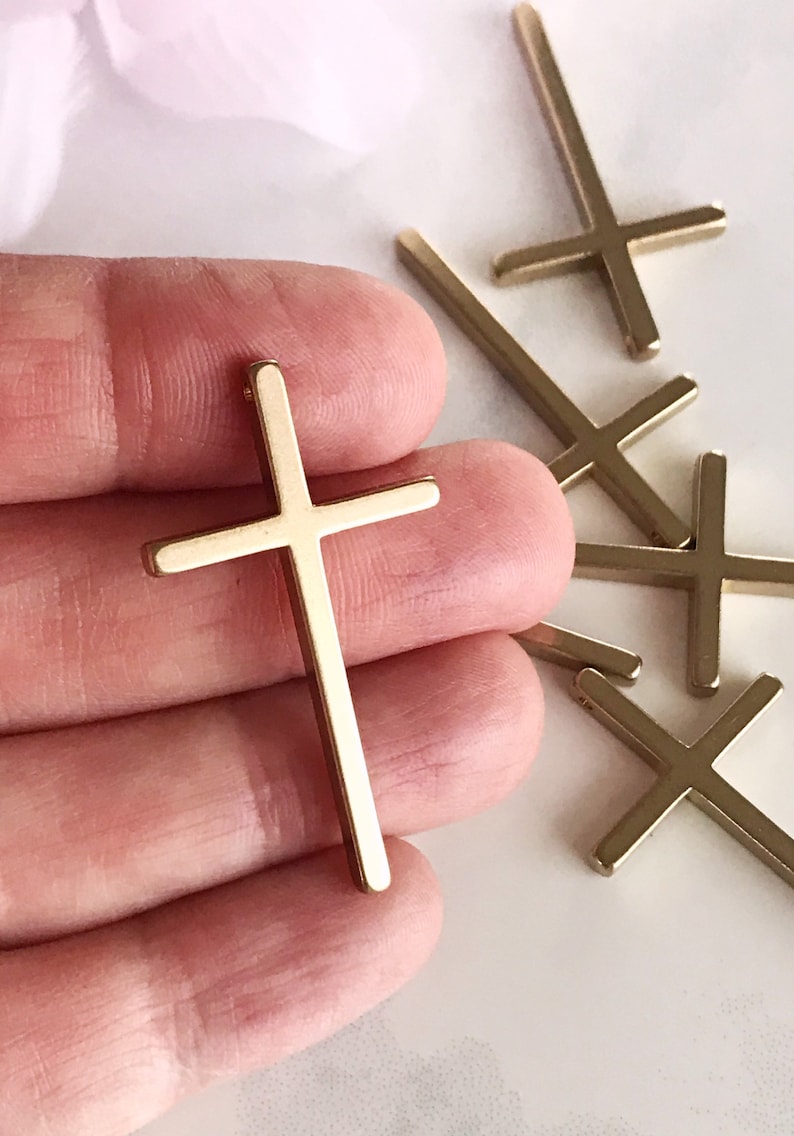 May include: A set of five gold-toned metal cross charms. The crosses are simple and elegant, with a flat, rectangular shape.