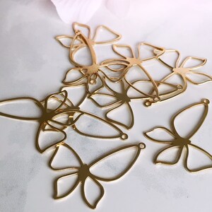 May include: A set of six gold-colored metal butterfly charms with openwork designs. The charms have a loop at the top for attaching to jewelry or other crafts.