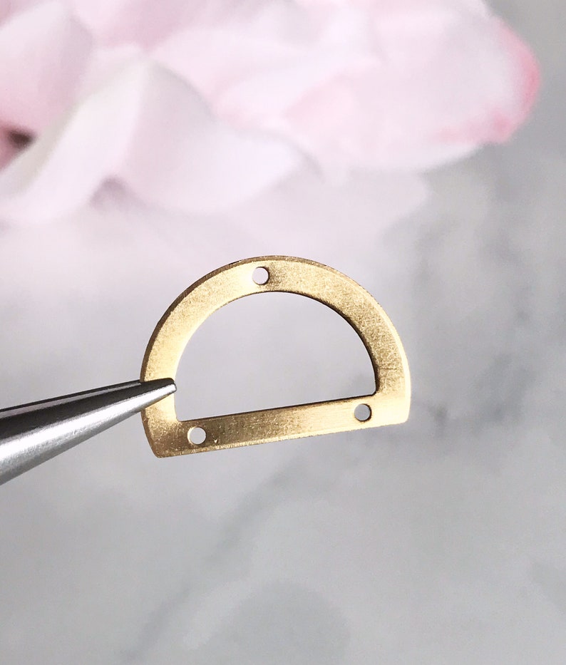 May include: A gold-colored metal D-ring with four holes for attaching jewelry or other crafts.