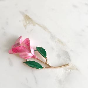 May include: A pink enamel rose brooch with green enamel leaves and a gold tone stem.