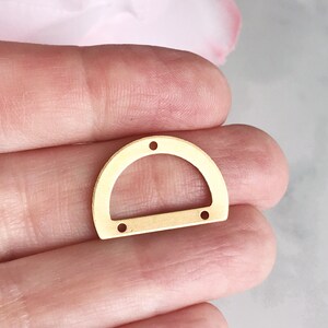May include: Gold metal half-circle shaped pendant with four holes for attaching to jewelry or other crafts.