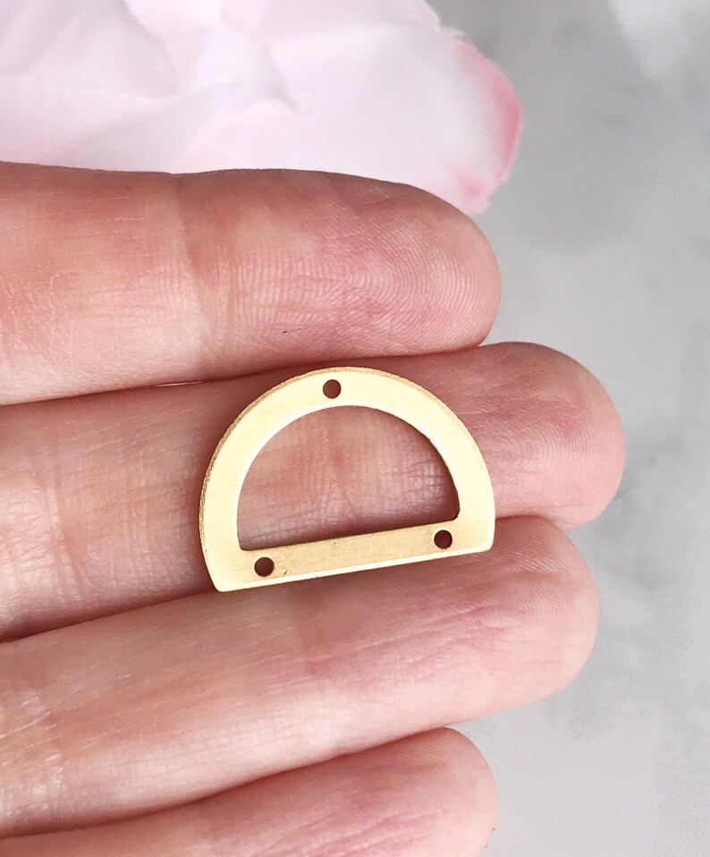 May include: Gold metal half-circle shaped pendant with four holes for attaching to jewelry or other crafts.