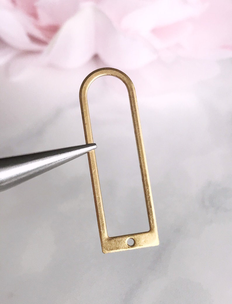 May include: Gold-toned metal frame with a rounded top and a small hole at the bottom. The frame is about 1.5 inches tall and 0.75 inches wide.