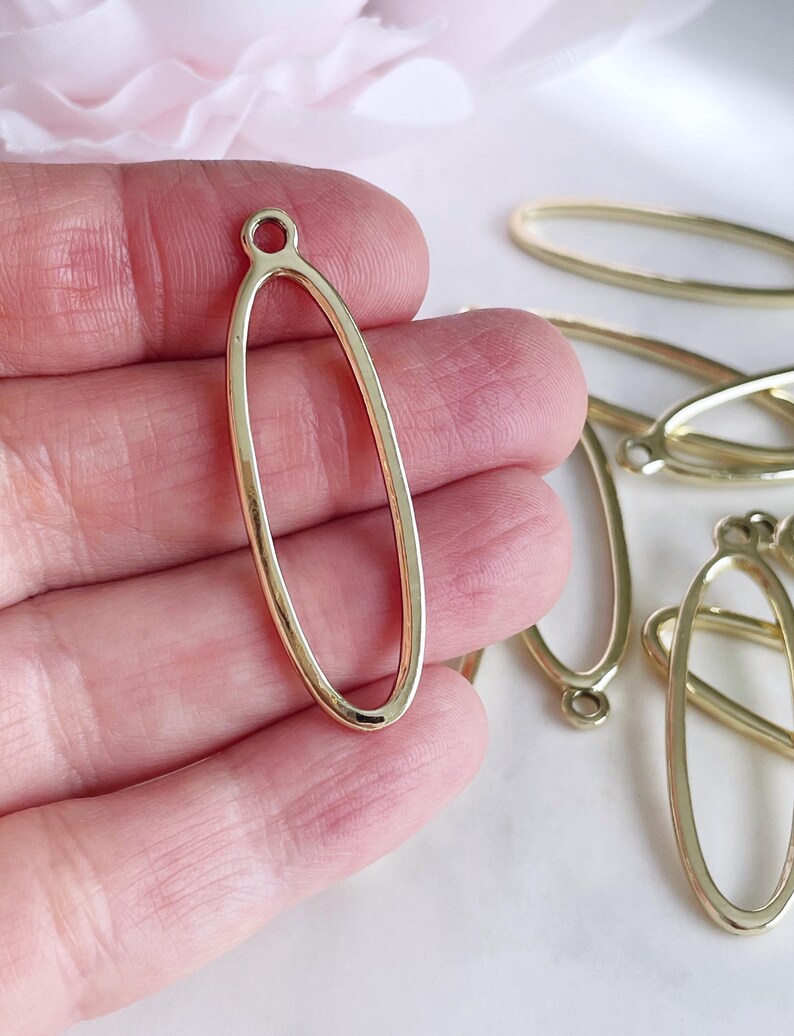May include: Gold oval-shaped metal pendant with a small loop at the top. The pendant is hollow and has a smooth, polished finish.
