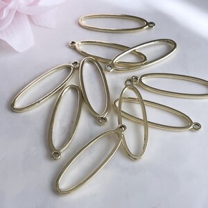 May include: A group of eight gold oval-shaped metal frames with a loop at the top. The frames are arranged in a pile on a white surface.