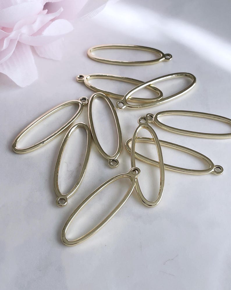 May include: A group of eight gold oval-shaped metal frames with a loop at the top. The frames are arranged in a pile on a white surface.