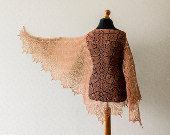 May include: A delicate lace shawl in shades of brown and peach, draped over a dress form. The shawl features an intricate floral pattern and a scalloped edge.