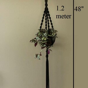 May include: Black macrame plant hanger with a green and purple plant in a brown pot. The hanger is 48 inches long and 1.2 metres long.