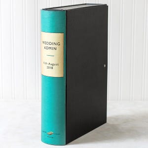 May include: A black binder with a teal spine featuring a cream-colored label. The label displays the text "WEDDING ADMIN" above a horizontal line and the date "11th August 2018". A small logo with the text "MB BINDERY ENGLAND" is at the bottom.