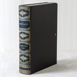 May include: A black document box with a spine designed to look like a vintage book. The spine is navy blue with gold filigree and the words "MORTGAGE" and "RAMBLERS WAY". The box has a small silver lock.