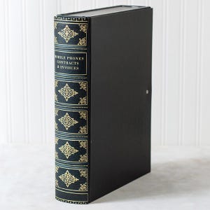 May include: Black binder with a decorative spine featuring gold and teal accents. The spine reads "MOBILE PHONES CONTRACTS & INVOICES". The binder has a lock and is likely for organizing documents.