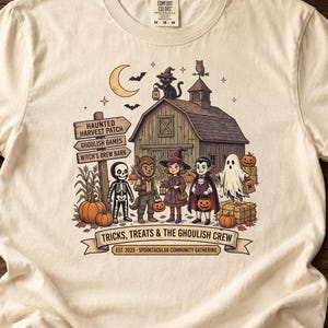 May include: An ivory t-shirt featuring a graphic of a barn, a crescent moon, and a group of costumed characters including a skeleton, werewolf, witch, vampire, and ghost. The text reads Haunted Harvest Patch, Ghoulish Games, Witch's Brew Barn, and Tricks, Treats & The Ghoulish Crew.