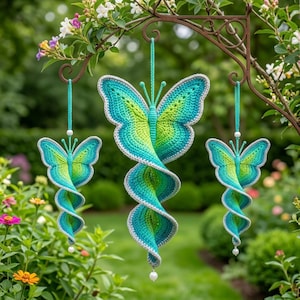 Pode incluir: Três ornamentos de crochê pendurados em forma de borboleta com cauda em espiral. Cada peça apresenta um padrão de cores degradê que vai do verde-limão no centro ao azul-petróleo nas bordas, com uma borda branca e uma pequena conta.
