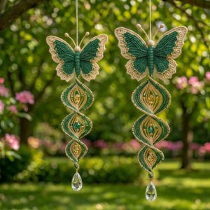 May include: Two macrame butterfly ornaments featuring dark green and beige cord, suspended by thin strings. Each butterfly is attached to a spiraling, twisted tail made of matching cord, accented with green and gold beads and a clear crystal drop.