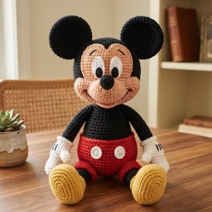 May include: A handcrafted crochet doll of a cartoon mouse character with large round black ears, a peach-colored face, and a black nose. The doll wears a black torso, red shorts with two white buttons, white gloves, and yellow shoes.