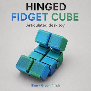 May include: A blue and green hinged fidget cube desk toy with articulated segments. The text HINGED FIDGET CUBE Articulated desk toy and Blue / Green finish is visible. The object consists of multiple connected square blocks in a gradient color.