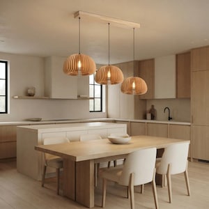 Peut inclure: Un trio de suspensions en bois clair avec des abat-jours arrondis à lattes, fixées à un support rectangulaire au plafond. Chaque luminaire comporte une ampoule centrale diffusant une lueur chaude, disposée en ligne au-dessus d'une table.