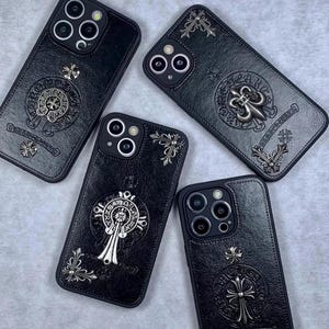 May include: Four black leather-textured phone cases featuring silver-toned metal emblems and decorative cross motifs. Each case displays unique circular embossed designs and metallic corner accents, surrounding the camera lens cutouts on the back.