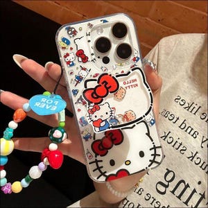 May include: A clear smartphone case featuring a Hello Kitty pattern with red bows and various character icons. The case includes a large Hello Kitty face graphic and a blue heart-shaped charm attached to a colorful beaded wrist strap.