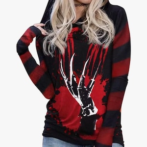 May include: A long-sleeved hooded shirt featuring a black and red striped pattern on the sleeves and a graphic print on the front. The graphic depicts a black hand with long, sharp, claw-like fingers against a red, splattered background.