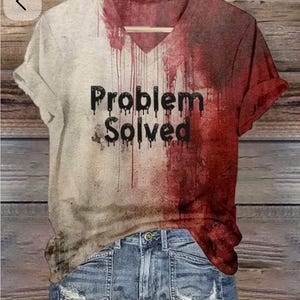 May include: A V-neck t-shirt featuring a split color design of off-white and deep red with a paint-splatter effect. The black text "Problem Solved" is printed across the center in a dripping font style. The shirt is paired with blue denim jeans.